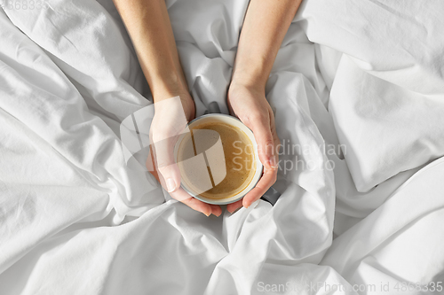 Image of hands of woman with cup of coffee in bed