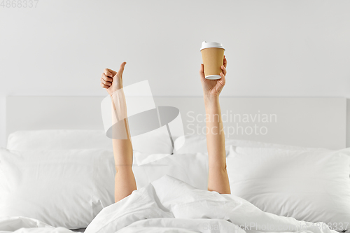 Image of woman with coffee lying in bed showing thumbs up