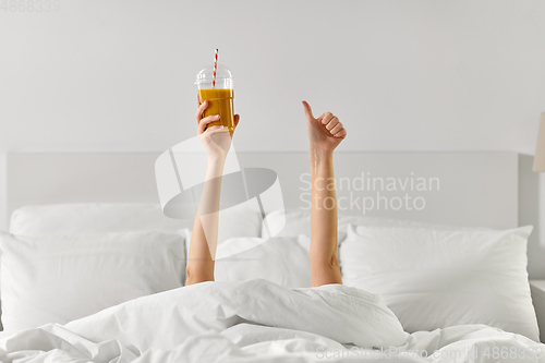 Image of hands of woman lying in bed with cup of juice