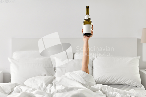 Image of hand of woman lying in bed with champagne