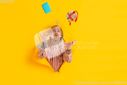 Image of Cheerful young man poses in torn yellow paper hole background, emotional and expressive