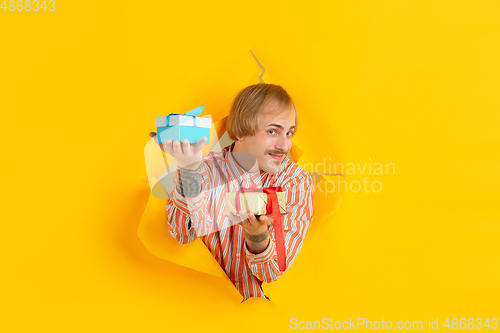 Image of Cheerful young man poses in torn yellow paper hole background, emotional and expressive