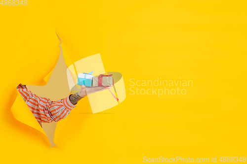 Image of Male hand giving gift in torn yellow paper hole background, celebration