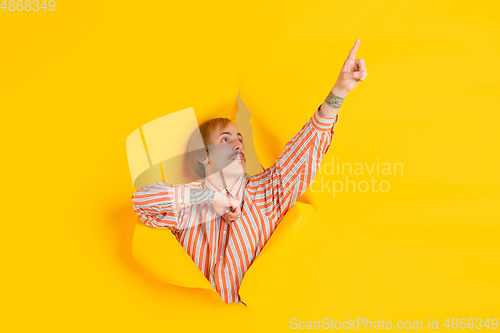 Image of Cheerful young man poses in torn yellow paper hole background, emotional and expressive