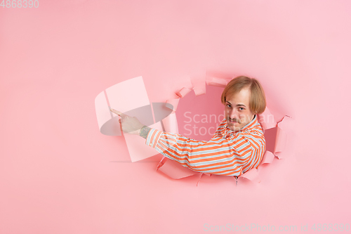 Image of Cheerful young man poses in torn coral paper hole background, emotional and expressive