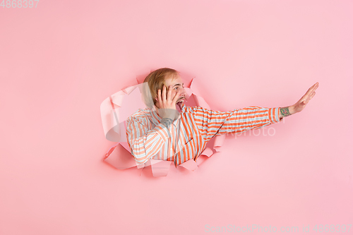 Image of Cheerful young man poses in torn coral paper hole background, emotional and expressive