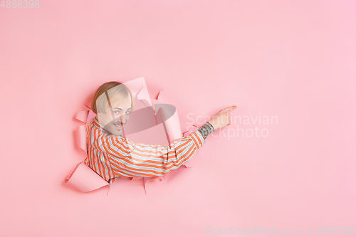 Image of Cheerful young man poses in torn coral paper hole background, emotional and expressive