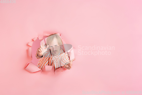 Image of Cheerful young man poses in torn coral paper hole background, emotional and expressive