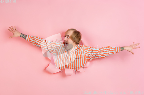 Image of Cheerful young man poses in torn coral paper hole background, emotional and expressive