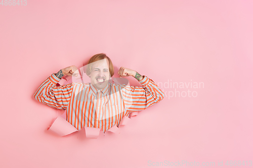 Image of Cheerful young man poses in torn coral paper hole background, emotional and expressive