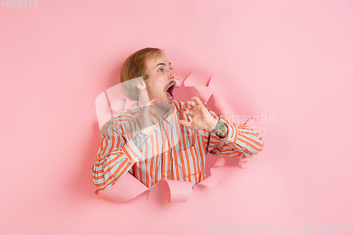 Image of Cheerful young man poses in torn coral paper hole background, emotional and expressive