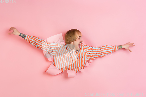 Image of Cheerful young man poses in torn coral paper hole background, emotional and expressive