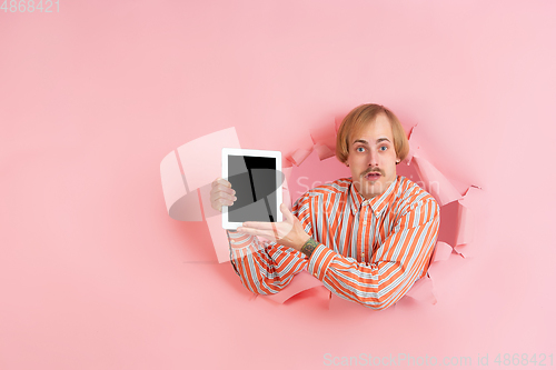 Image of Cheerful young man poses in torn coral paper hole background, emotional and expressive