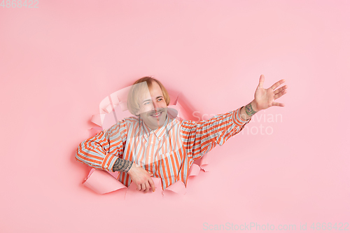 Image of Cheerful young man poses in torn coral paper hole background, emotional and expressive