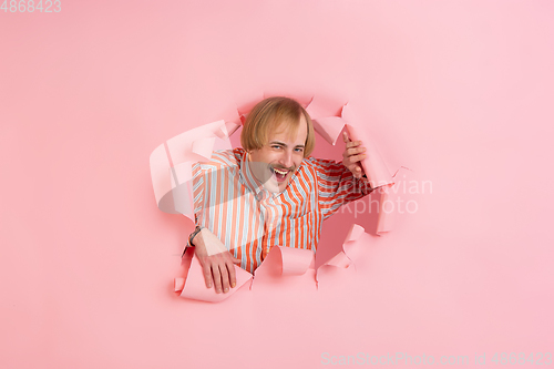 Image of Cheerful young man poses in torn coral paper hole background, emotional and expressive