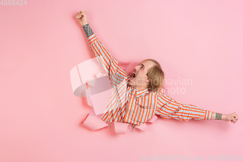 Image of Cheerful young man poses in torn coral paper hole background, emotional and expressive