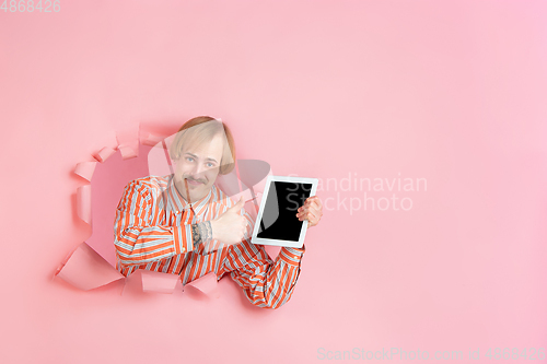 Image of Cheerful young man poses in torn coral paper hole background, emotional and expressive