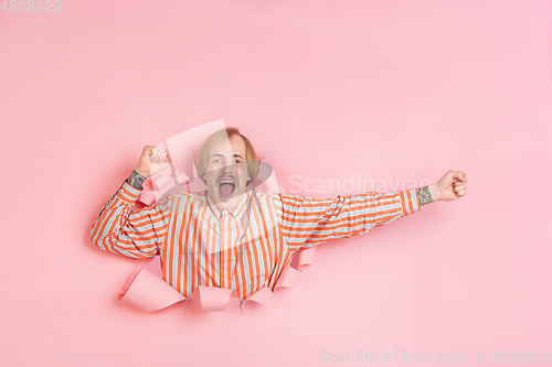 Image of Cheerful young man poses in torn coral paper hole background, emotional and expressive