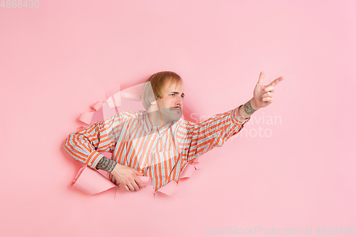 Image of Cheerful young man poses in torn coral paper hole background, emotional and expressive