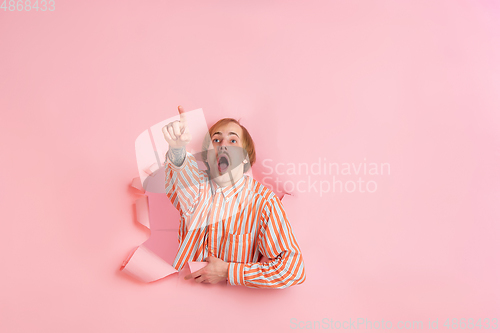 Image of Cheerful young man poses in torn coral paper hole background, emotional and expressive