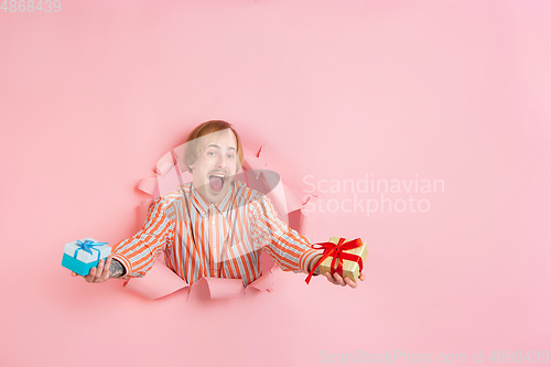 Image of Cheerful young man poses in torn coral paper hole background, emotional and expressive