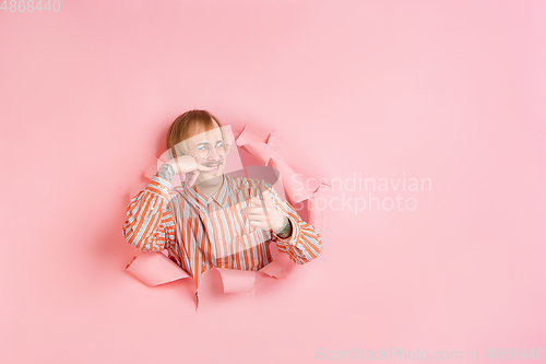 Image of Cheerful young man poses in torn coral paper hole background, emotional and expressive