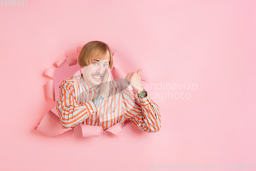 Image of Cheerful young man poses in torn coral paper hole background, emotional and expressive