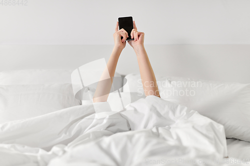 Image of hands of woman lying in bed with smartphone