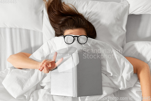 Image of woman lying in bed with book and glasses