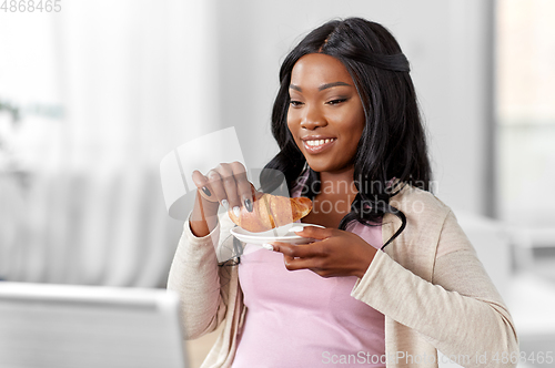 Image of woman with laptop eating croissant at home office