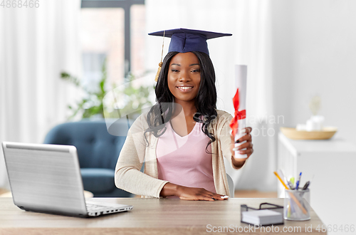 Image of graduate student with laptop and diploma at home