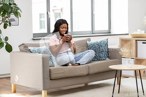 Image of happy african woman drinking tea or coffee at home