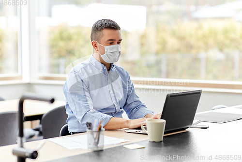 Image of man in mask with laptop working at home office