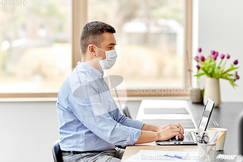 Image of man in mask with laptop working at home office