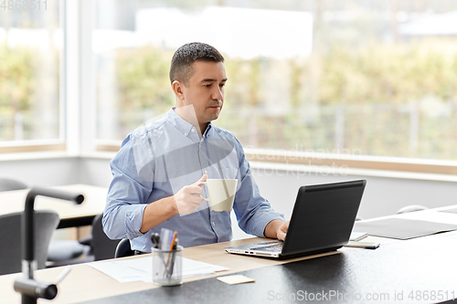 Image of man with laptop drinking coffee at home office