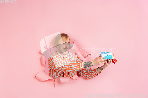 Image of Cheerful young man poses in torn coral paper hole background, emotional and expressive