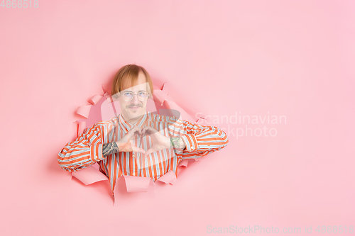 Image of Cheerful young man poses in torn coral paper hole background, emotional and expressive