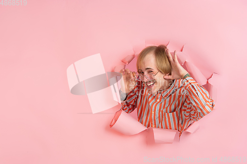 Image of Cheerful young man poses in torn coral paper hole background, emotional and expressive