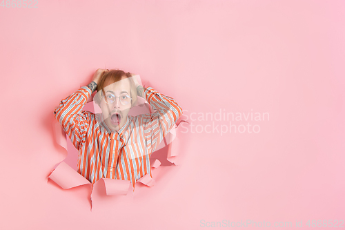 Image of Cheerful young man poses in torn coral paper hole background, emotional and expressive