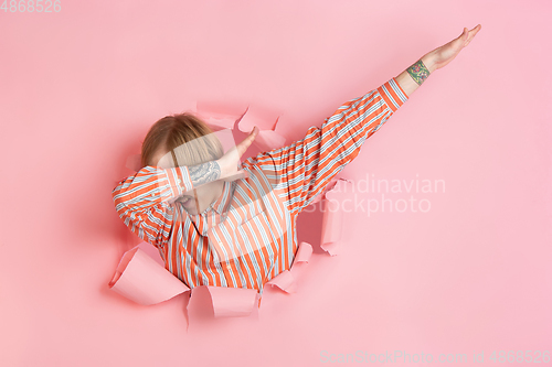 Image of Cheerful young man poses in torn coral paper hole background, emotional and expressive