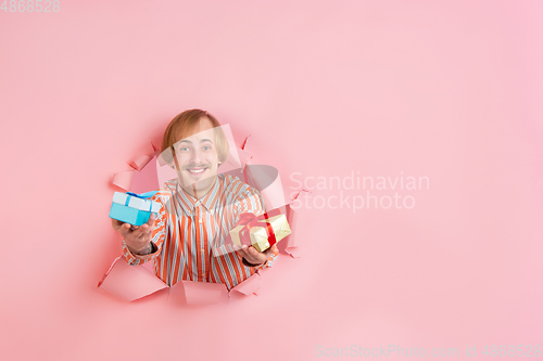 Image of Cheerful young man poses in torn coral paper hole background, emotional and expressive