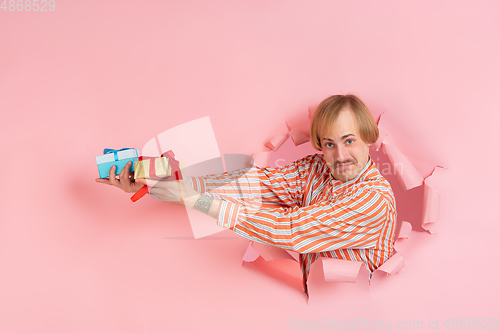 Image of Cheerful young man poses in torn coral paper hole background, emotional and expressive