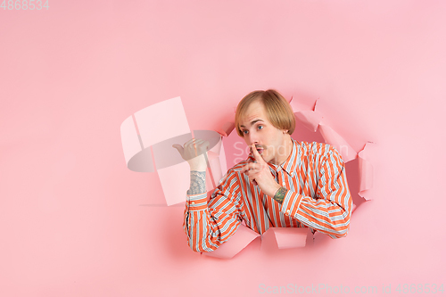 Image of Cheerful young man poses in torn coral paper hole background, emotional and expressive