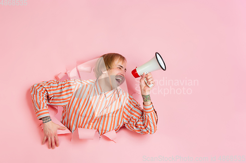 Image of Cheerful young man poses in torn coral paper hole background, emotional and expressive