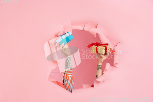 Image of Male hand giving gift in torn coral paper hole background, celebration