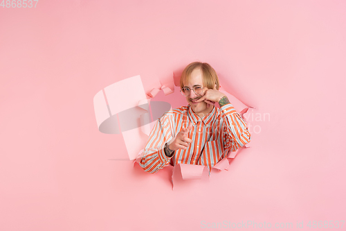 Image of Cheerful young man poses in torn coral paper hole background, emotional and expressive