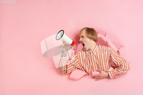 Image of Cheerful young man poses in torn coral paper hole background, emotional and expressive