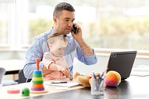 Image of father with baby calling on phone at home office