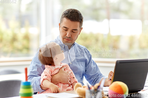 Image of father with baby working on laptop at home office