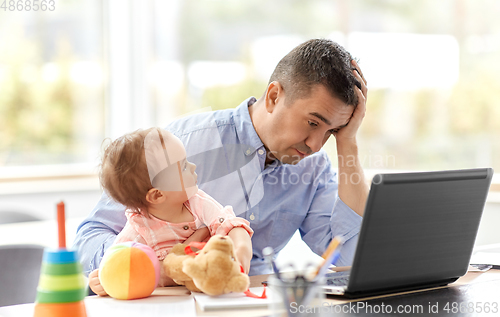 Image of father with baby working on laptop at home office